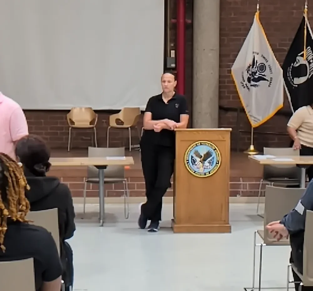 Carmen &ldquo;The Momba&rdquo; Gulliksen at the podium, addressing an audience at a Department of Veterans Affairs facility